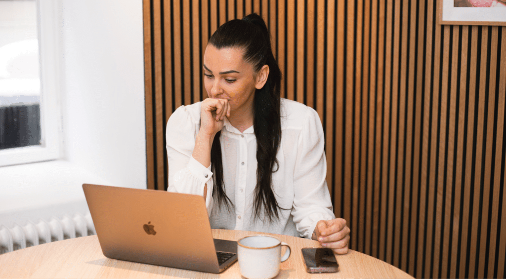 En kvinna med mörkt lång hår som sitter med datorn framför sig och ser fundersam ut
